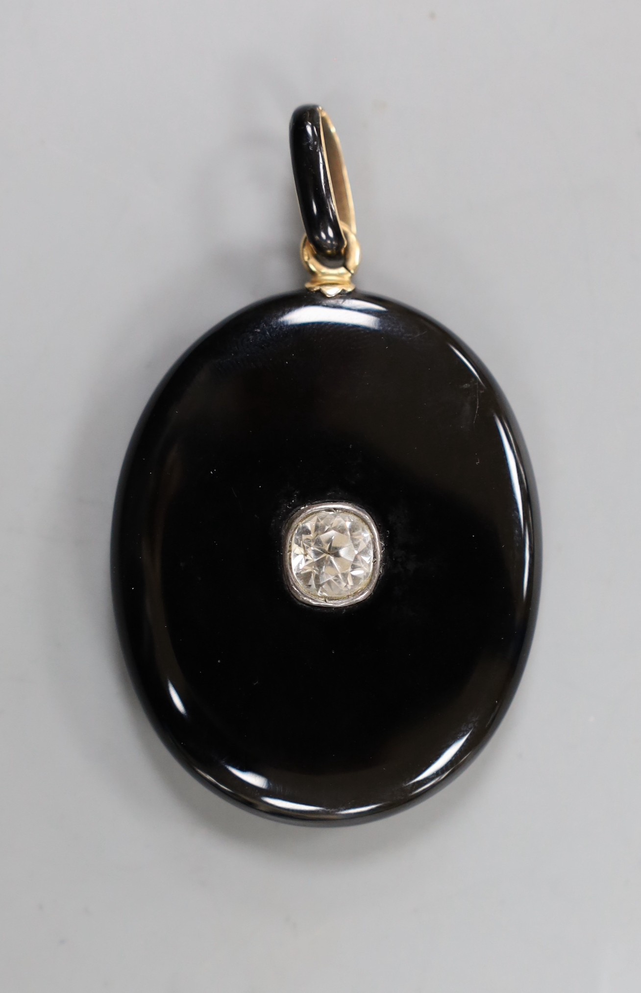 A Victorian black enamelled yellow metal oval locket, set with an old cut white sapphire, overall 62mm.